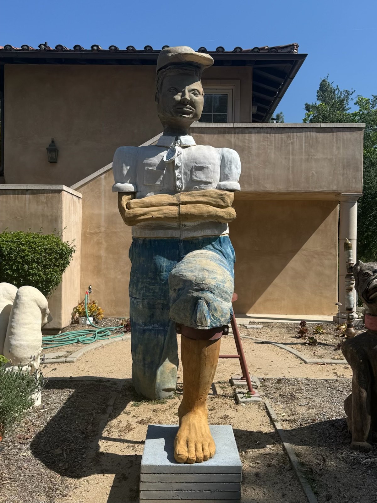 Monumental ceramic figure with crossed arms, blue trousers and one colossal bare foot on a plinth
