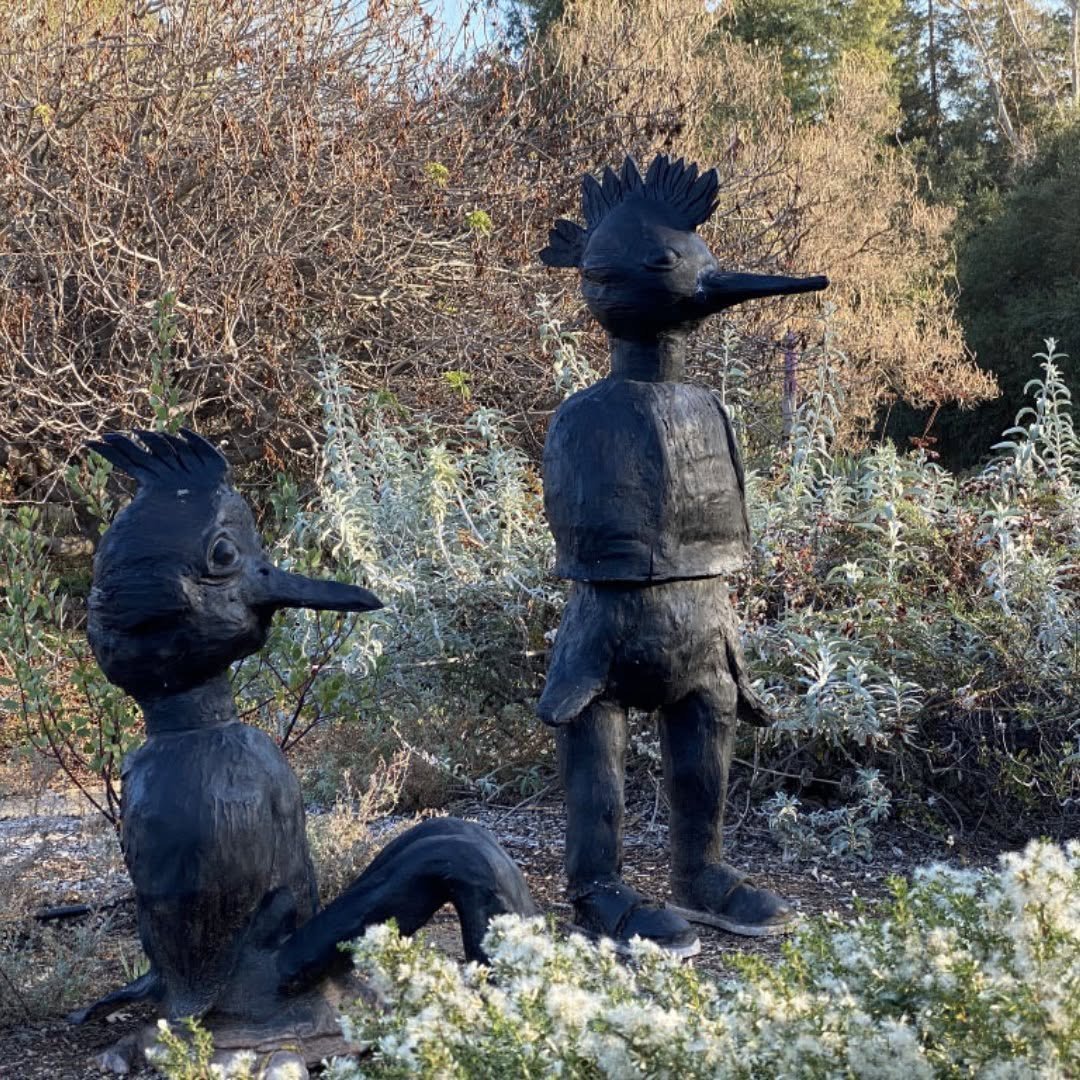 Two black ceramic bird figures with crests standing among sage and native shrubs