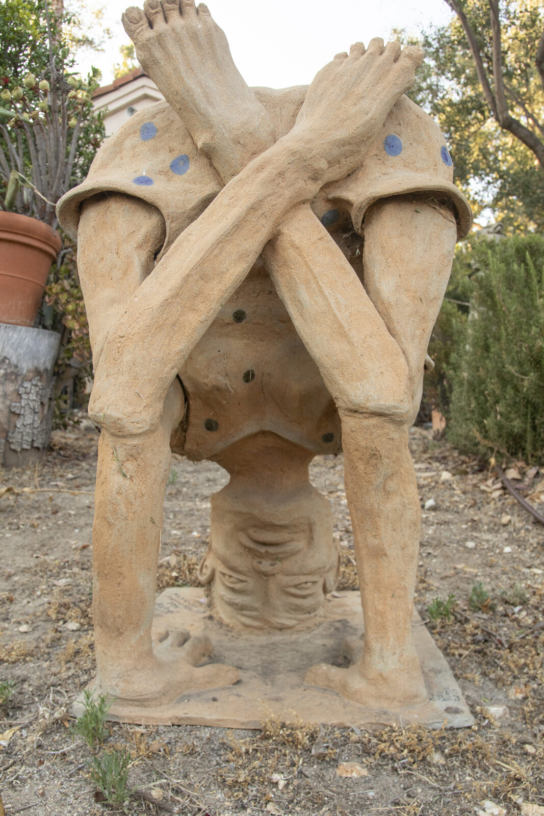 Ceramic figure balancing upside down in a handstand with bare feet crossed overhead