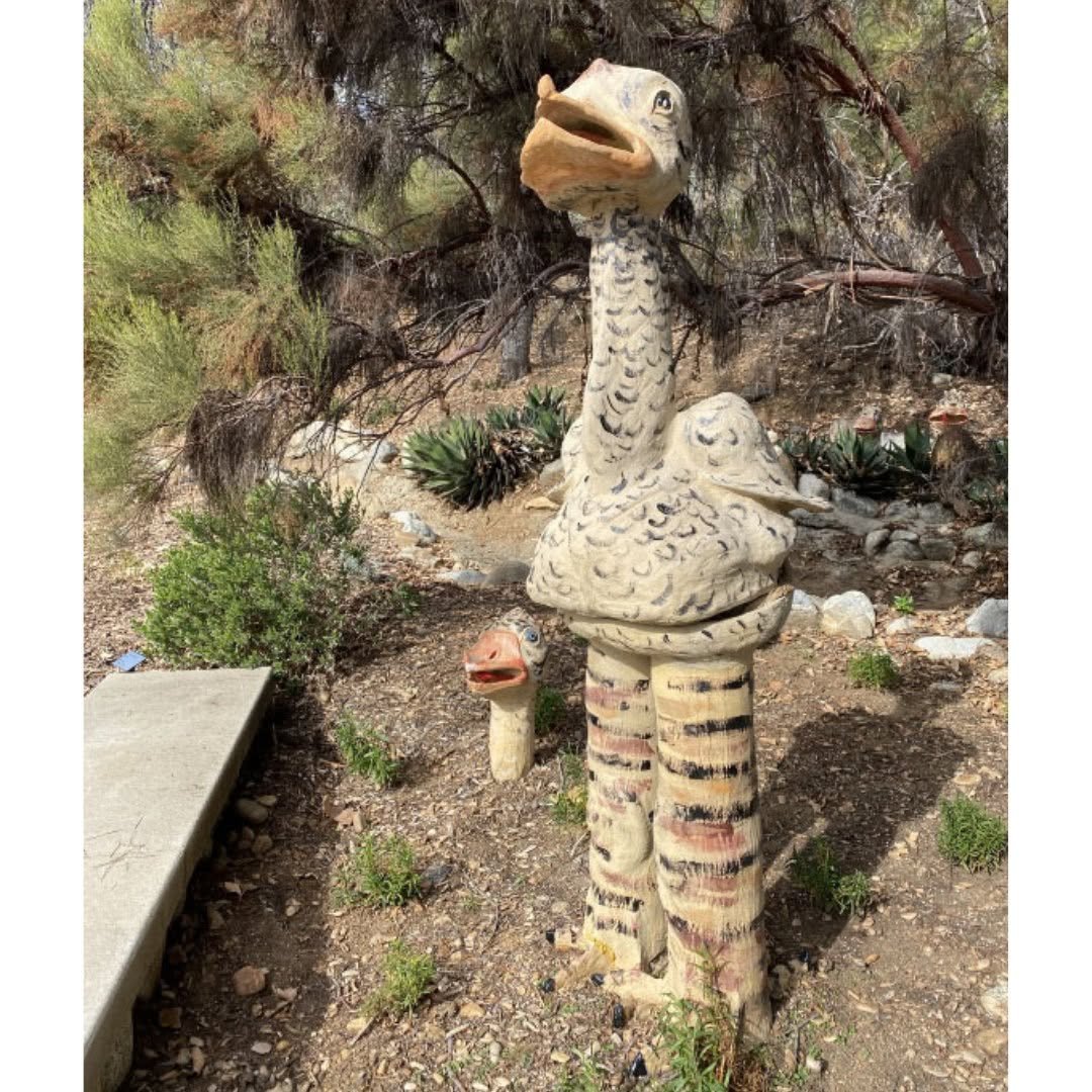 Tall ceramic ostrich-like bird with painted feathers and striped legs standing in native garden