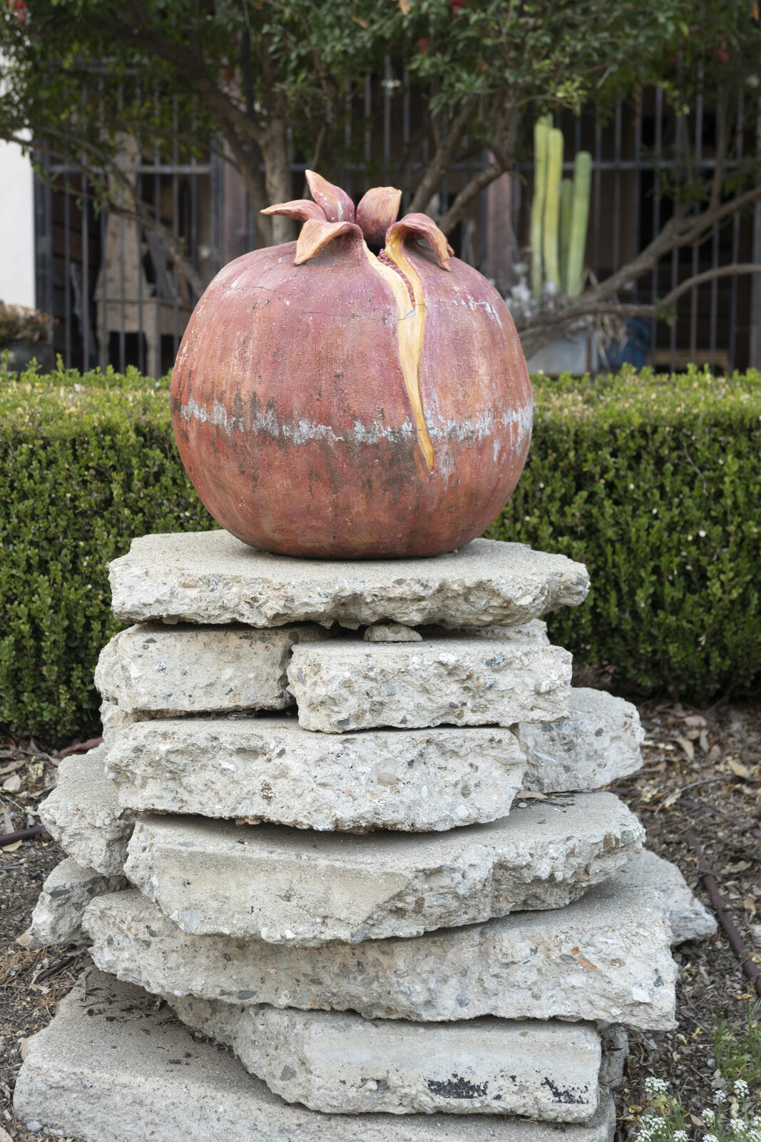 Split ceramic pomegranate resting on a stacked stone plinth in a courtyard garden