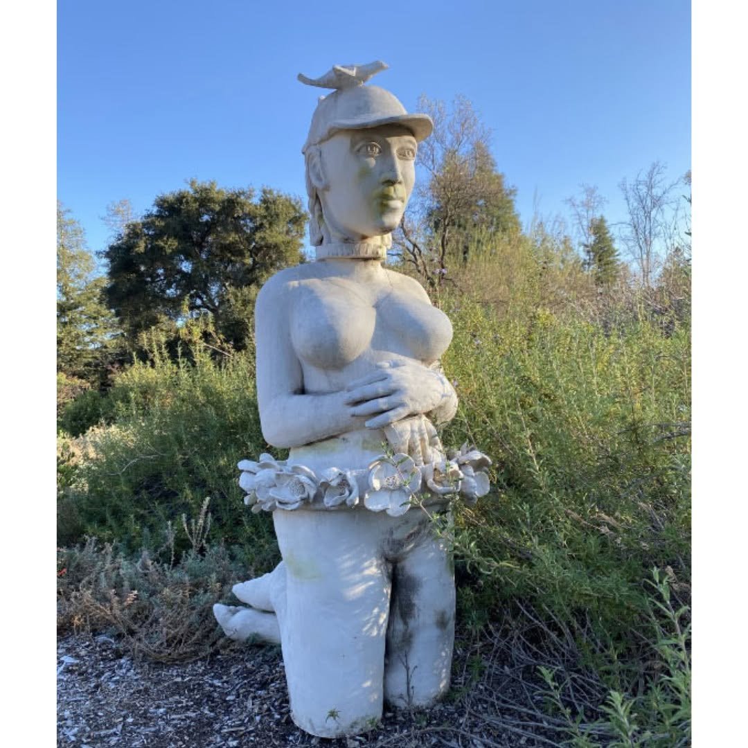 White ceramic female figure in a cap with a bird perched on top and a wreath of flowers at the waist