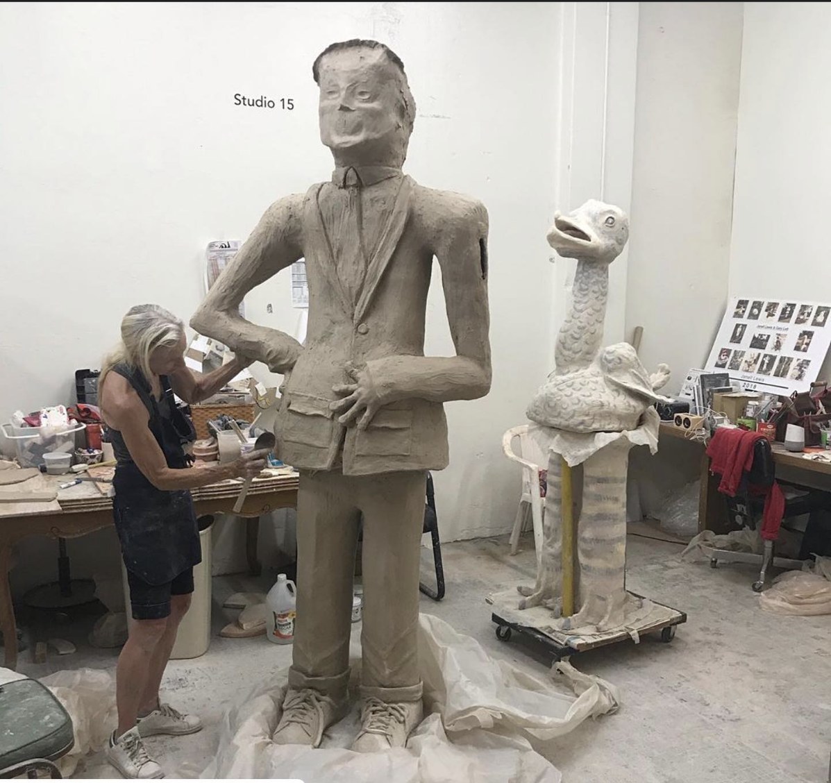 Janell Lewis working on a life-size clay figure in her studio, with a large bird sculpture nearby