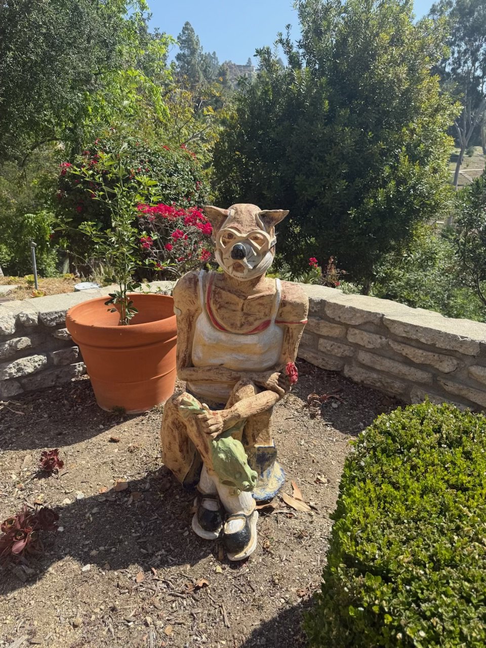 Seated ceramic wolf figure in a white tank top holding a rose, with a lizard on its knee